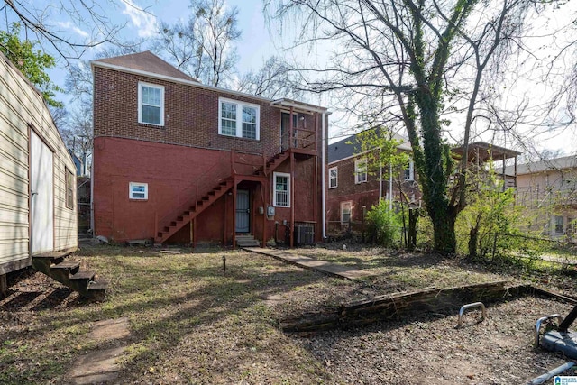 rear view of property featuring entry steps, brick siding, stairs, and fence