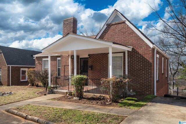 bungalow-style house featuring covered porch, brick siding, and a chimney