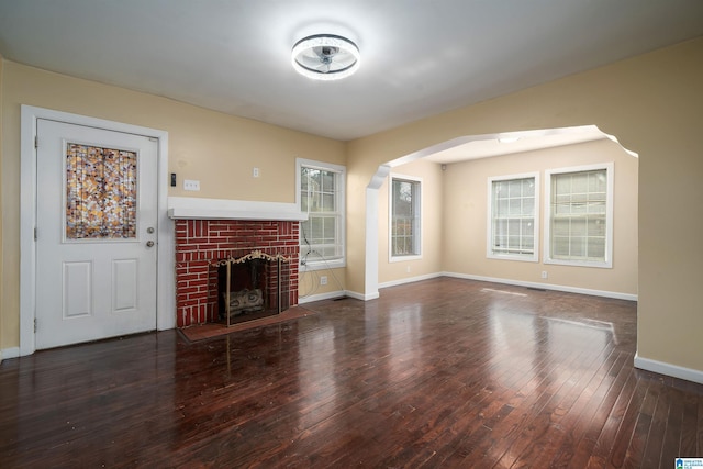 unfurnished living room with plenty of natural light, arched walkways, a fireplace, and hardwood / wood-style flooring