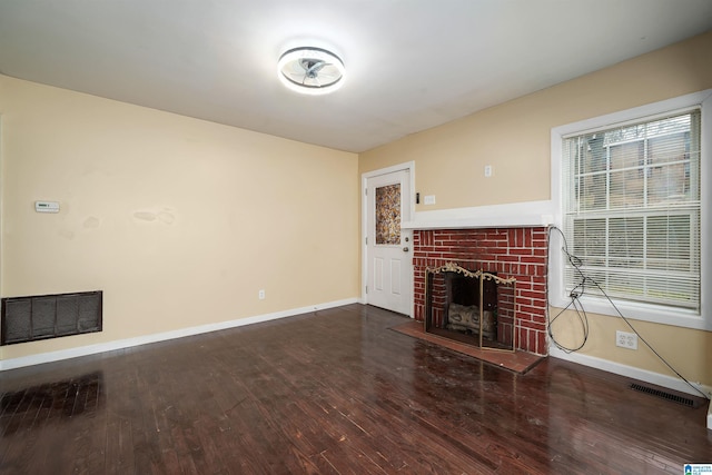 unfurnished living room with visible vents, baseboards, a brick fireplace, and wood finished floors