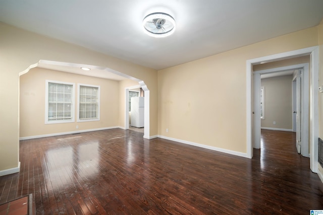 unfurnished room with hardwood / wood-style flooring, baseboards, and arched walkways