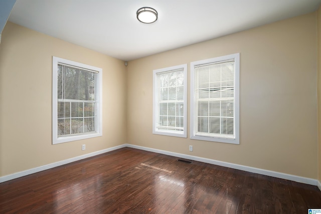 empty room with visible vents, dark wood-type flooring, and baseboards