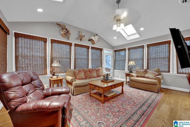 living area featuring vaulted ceiling with skylight, recessed lighting, a ceiling fan, baseboards, and light wood finished floors