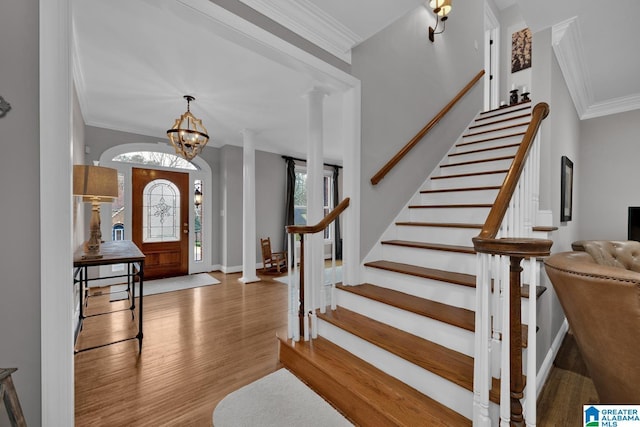 entryway featuring wood finished floors, baseboards, stairs, ornamental molding, and decorative columns