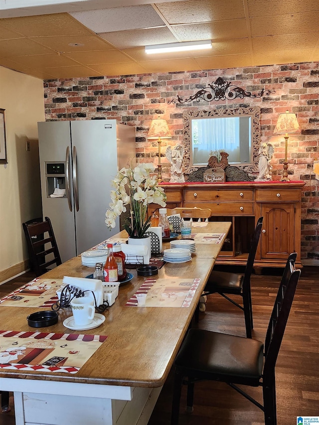 dining area featuring brick wall, a drop ceiling, dark wood finished floors, and baseboards