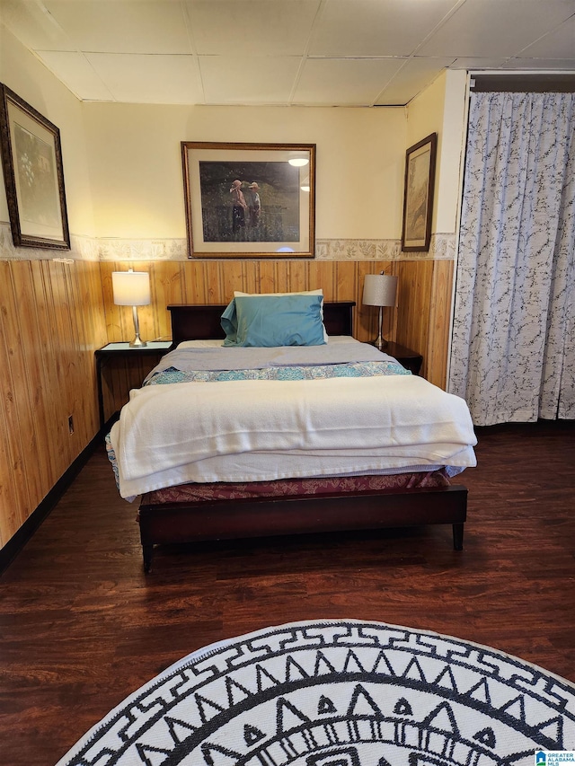 bedroom with a drop ceiling, wood walls, wainscoting, and wood finished floors