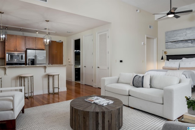 living area with baseboards, visible vents, wood finished floors, and ceiling fan with notable chandelier