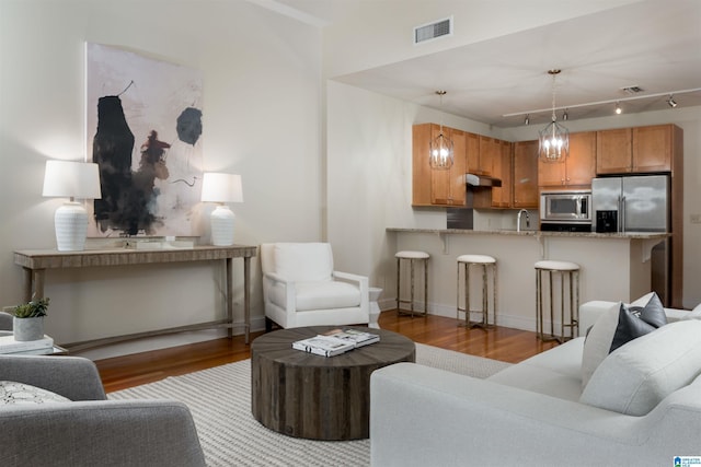 living room with a notable chandelier, wood finished floors, visible vents, and baseboards