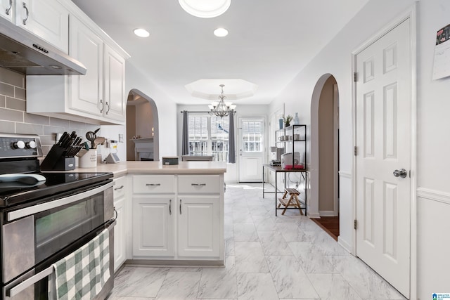 kitchen with range with two ovens, a raised ceiling, white cabinets, a peninsula, and under cabinet range hood