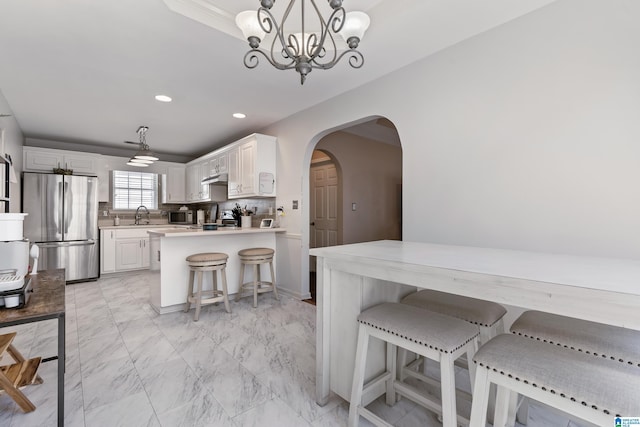 kitchen featuring arched walkways, marble finish floor, stainless steel appliances, backsplash, and under cabinet range hood