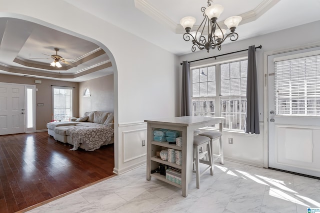 dining space featuring a tray ceiling, arched walkways, crown molding, and ceiling fan with notable chandelier