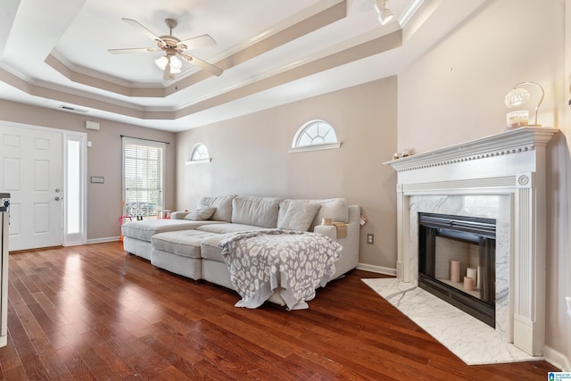 living area featuring a high end fireplace, a raised ceiling, crown molding, and wood finished floors