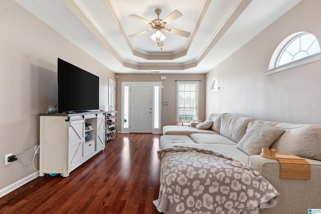 living room featuring baseboards, a raised ceiling, ceiling fan, ornamental molding, and dark wood-style flooring