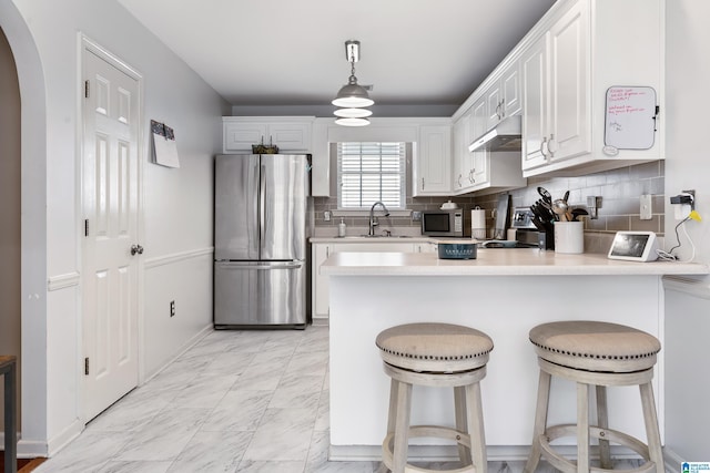 kitchen featuring arched walkways, appliances with stainless steel finishes, marble finish floor, under cabinet range hood, and a sink