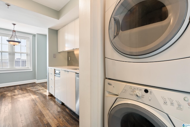 laundry area with stacked washer and clothes dryer, dark wood finished floors, baseboards, and laundry area