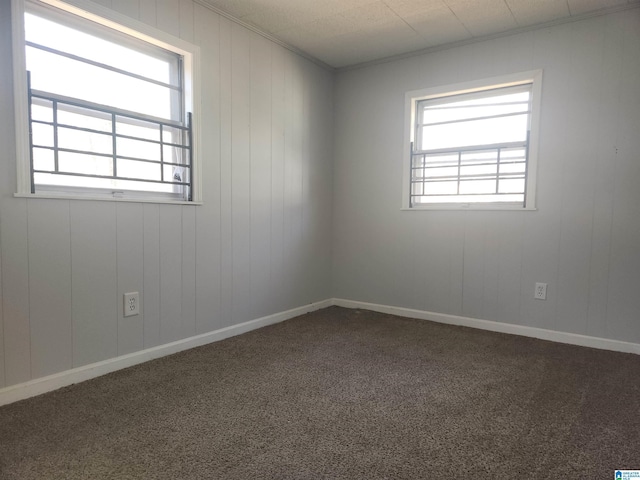 unfurnished room featuring dark carpet, ornamental molding, and plenty of natural light