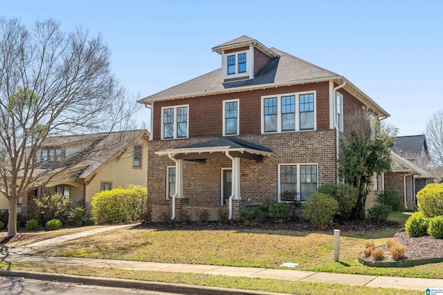 american foursquare style home with brick siding, a front yard, and a shingled roof