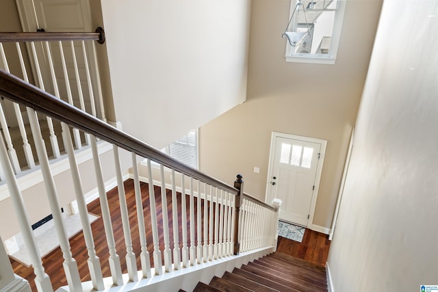 staircase featuring a high ceiling, baseboards, and wood finished floors