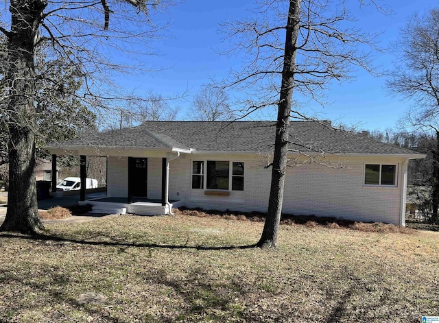 view of front of property with brick siding, covered porch, a front lawn, and roof with shingles