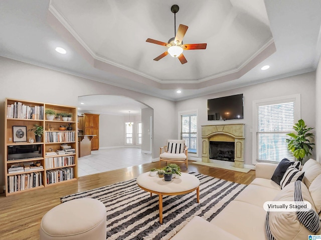 living room featuring light wood finished floors, a tray ceiling, arched walkways, a high end fireplace, and ornamental molding