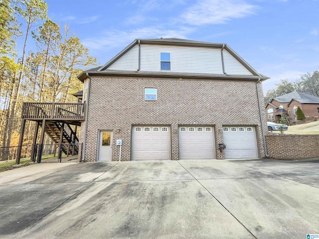 view of side of property with a wooden deck, an attached garage, stairs, concrete driveway, and brick siding