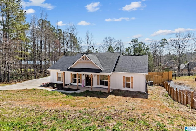 view of front of home with a front lawn, fence, covered porch, roof with shingles, and concrete driveway