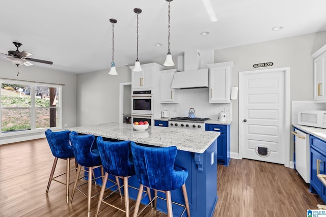 kitchen featuring custom range hood, blue cabinetry, wood finished floors, white cabinetry, and white appliances