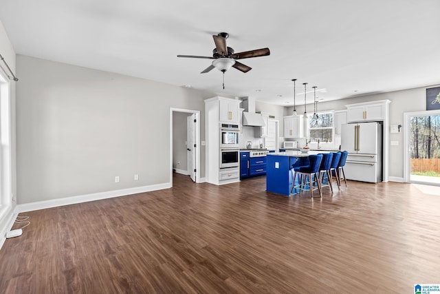 kitchen featuring wall chimney range hood, a kitchen breakfast bar, white cabinets, white appliances, and blue cabinets