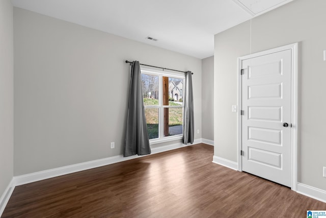 empty room featuring attic access, wood finished floors, visible vents, and baseboards