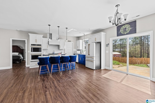 kitchen with a center island, an inviting chandelier, custom exhaust hood, white appliances, and white cabinetry