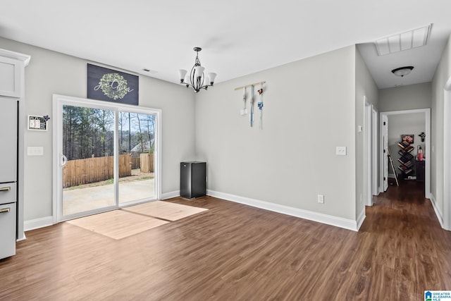 unfurnished dining area featuring visible vents, baseboards, an inviting chandelier, and wood finished floors