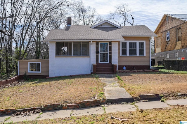 bungalow-style house with a shingled roof, entry steps, brick siding, and a chimney