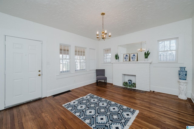 entrance foyer featuring a notable chandelier, visible vents, a brick fireplace, a textured ceiling, and wood finished floors