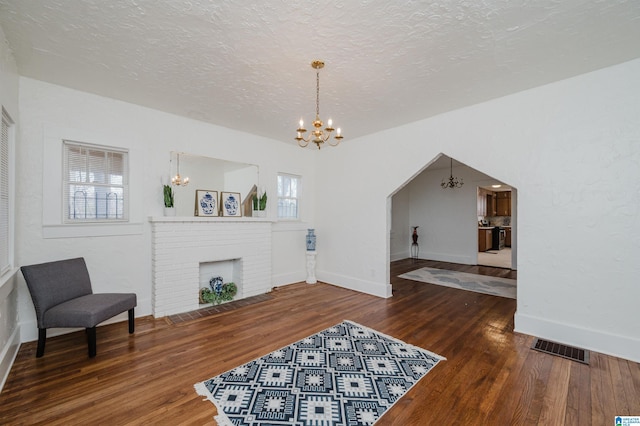 sitting room with visible vents, wood finished floors, a textured ceiling, a brick fireplace, and a notable chandelier