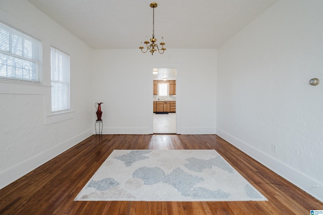 spare room with baseboards, dark wood-type flooring, and an inviting chandelier