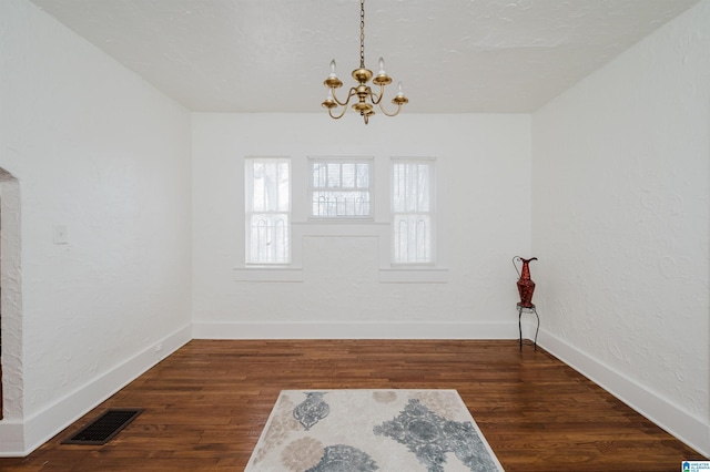 unfurnished room with a chandelier, wood finished floors, visible vents, and baseboards