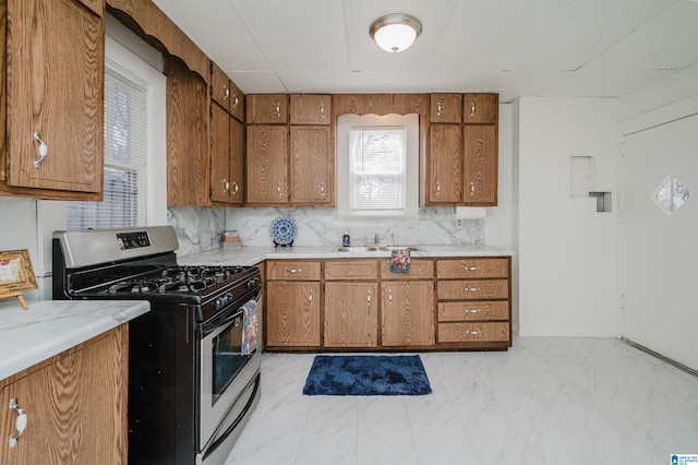 kitchen with stainless steel gas range oven, brown cabinets, marble finish floor, light countertops, and a sink