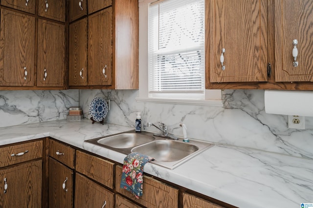 kitchen featuring brown cabinets, decorative backsplash, light countertops, and a sink