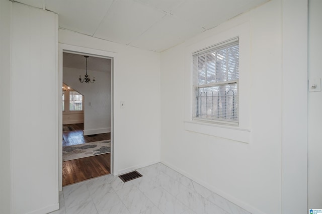 empty room featuring marble finish floor, visible vents, a notable chandelier, and baseboards