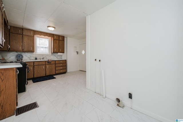 kitchen featuring visible vents, marble finish floor, black stove, light countertops, and backsplash