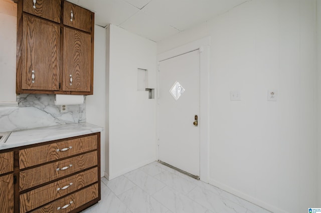 kitchen featuring marble finish floor, brown cabinetry, light countertops, and decorative backsplash