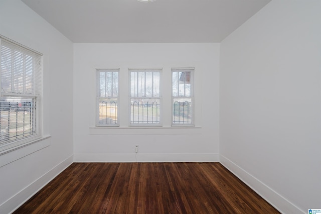 empty room featuring a wealth of natural light, dark wood-style flooring, and baseboards