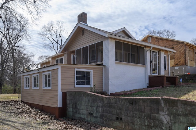 view of side of property featuring a sunroom, brick siding, fence, and a chimney