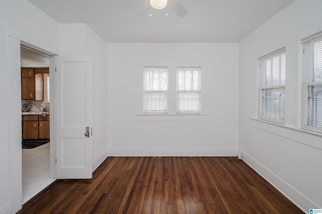 spare room featuring dark wood-type flooring, plenty of natural light, a ceiling fan, and baseboards