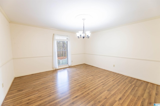 spare room featuring a chandelier, crown molding, baseboards, and wood finished floors