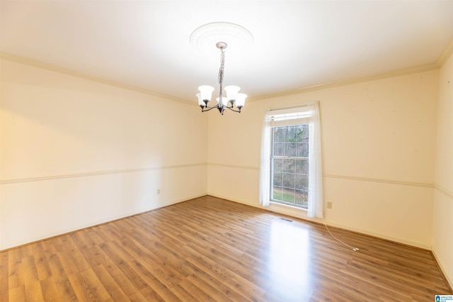 empty room featuring visible vents, an inviting chandelier, ornamental molding, wood finished floors, and baseboards