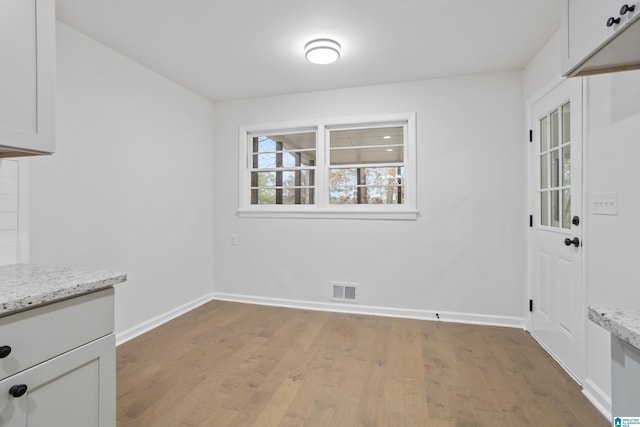 unfurnished dining area featuring light wood-style floors, baseboards, and visible vents