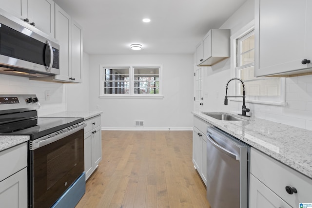 kitchen featuring a sink, baseboards, appliances with stainless steel finishes, light wood-type flooring, and decorative backsplash