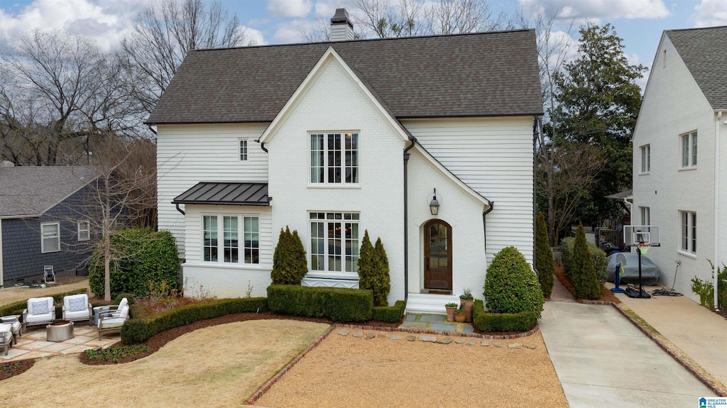 view of front of house featuring brick siding, a standing seam roof, a chimney, metal roof, and a patio