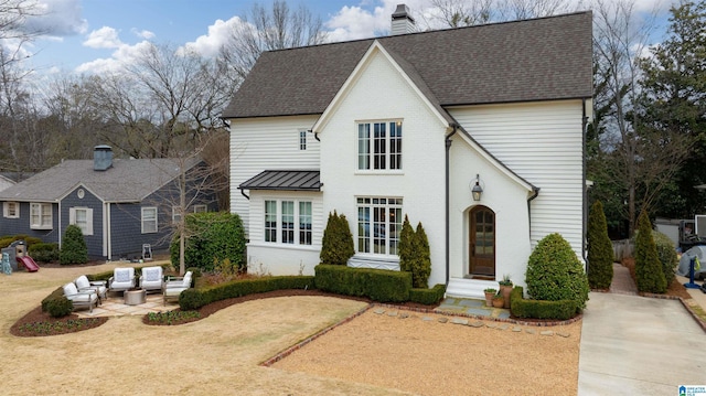 view of front facade with an outdoor hangout area, brick siding, a patio, and a chimney